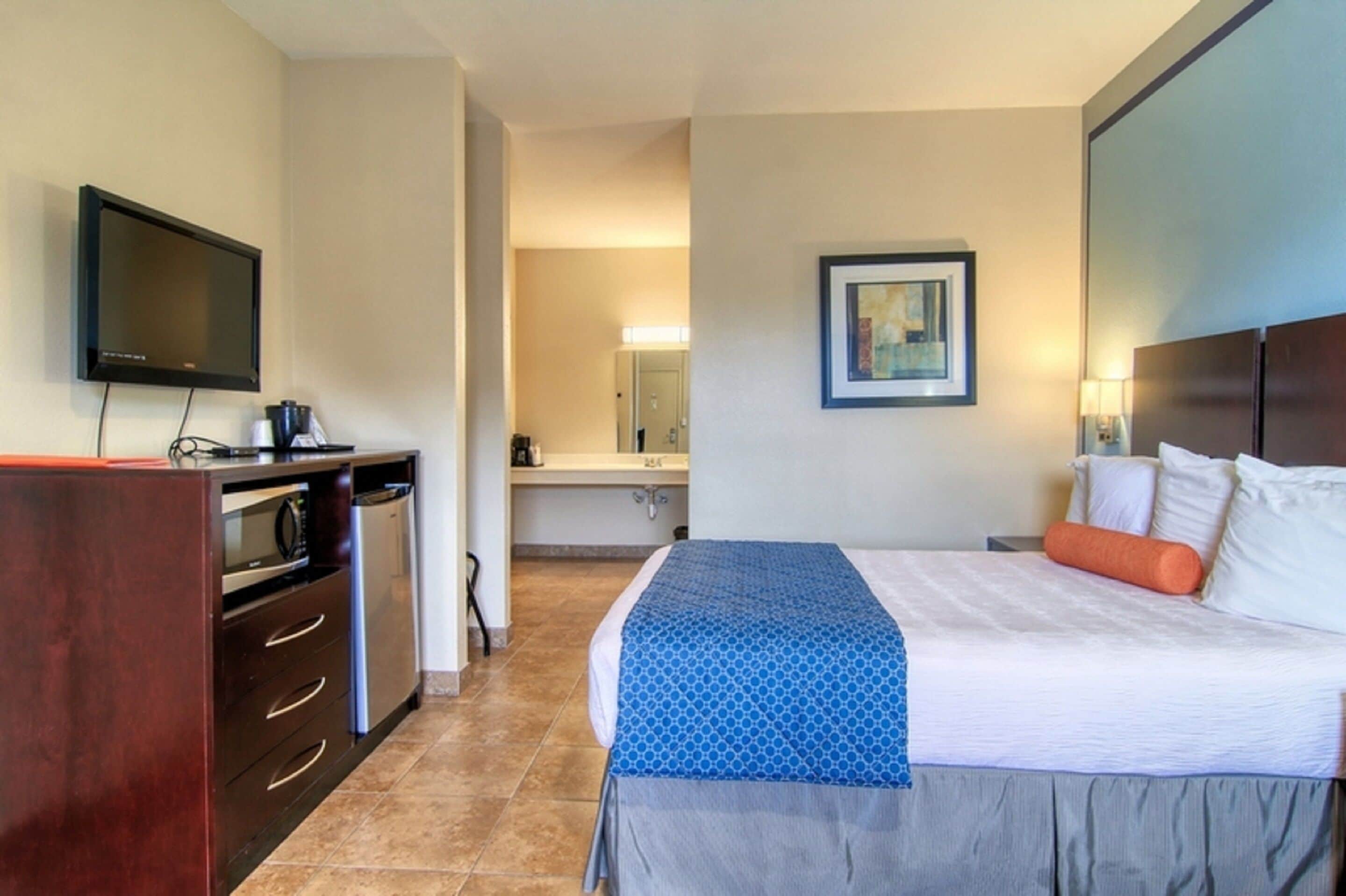 Habitación de hotel con cama, televisor, escritorio con microondas y baño a la vista.