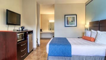Habitación de hotel con cama, televisor, escritorio con microondas y baño a la vista.