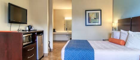 A hotel room with a bed, a TV, a desk with a microwave, and a bathroom visible in the background.