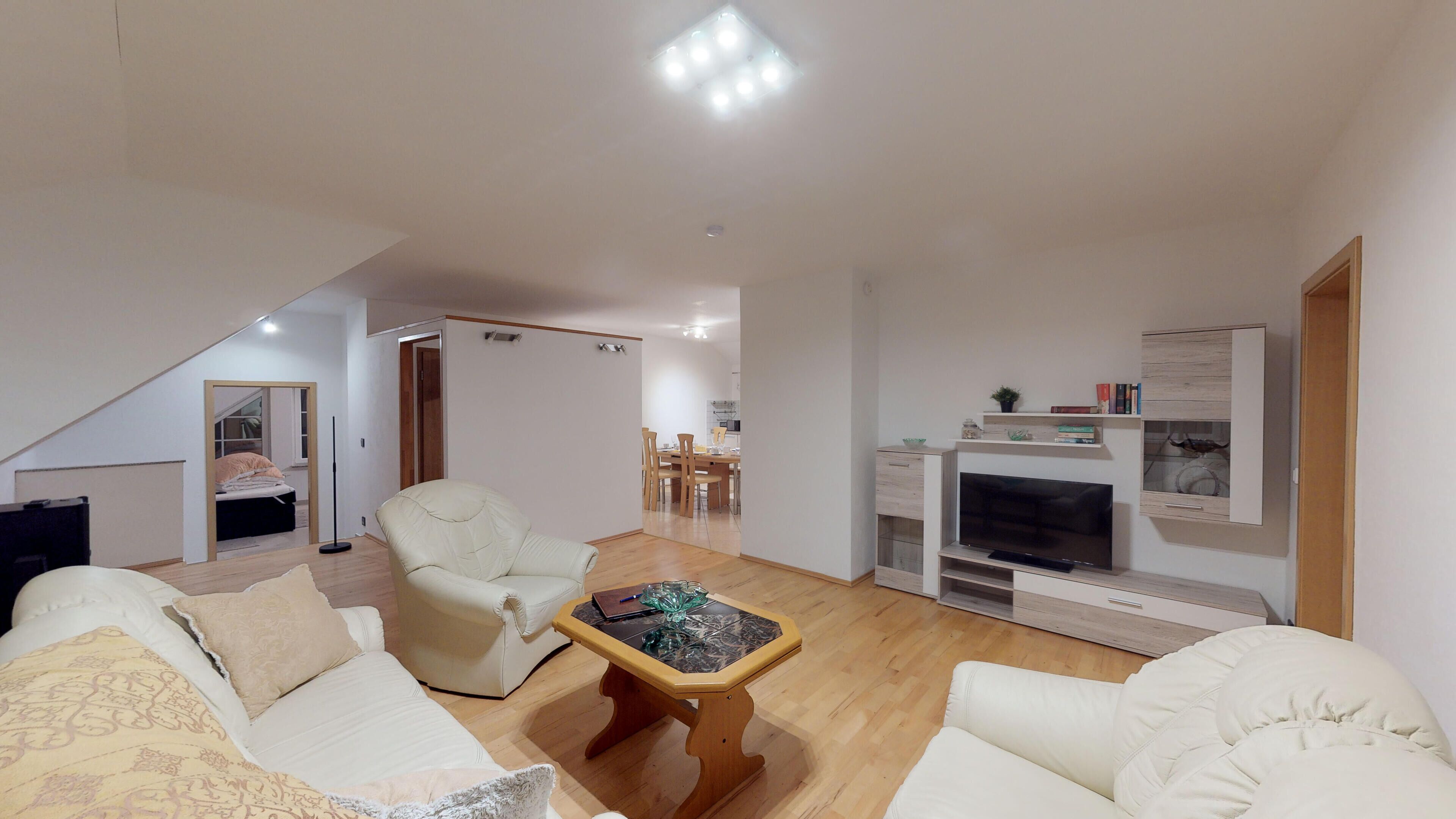 A modern living room with a sofa, armchair, and coffee table. There is a dining area in the background with a table and chairs.