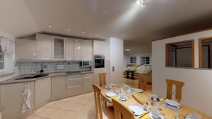 Una cocina moderna con electrodomésticos integrados, un comedor con mesa de madera para cuatro personas y una sala de estar acogedora con sofá y ventana.