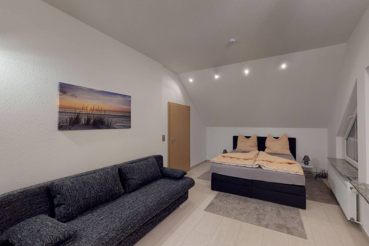 A bedroom with a bed, a sofa, a painting, and a window.