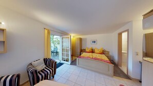 Un dormitorio con cama, una silla, un armario y una puerta que da a un balcón.
