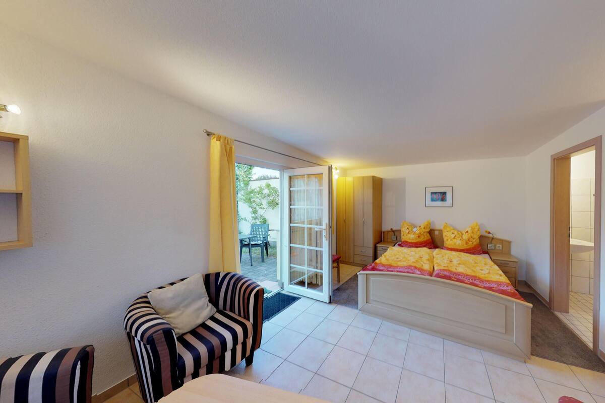 A bedroom with a bed, a chair, a wardrobe, and a door leading to a balcony.