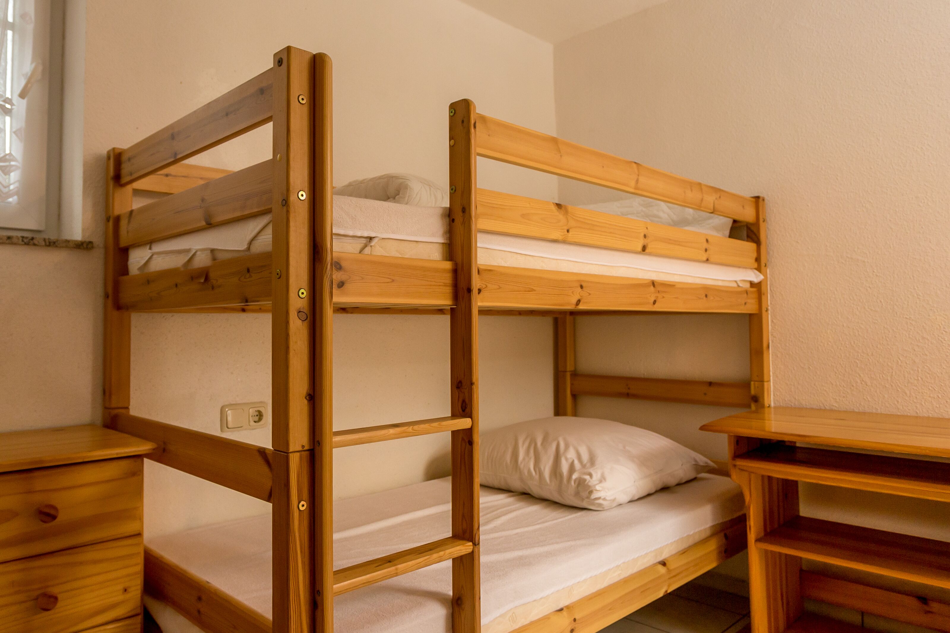 Ein Stockbett mit Holzrahmen, ein Nachttisch und eine Kommode.