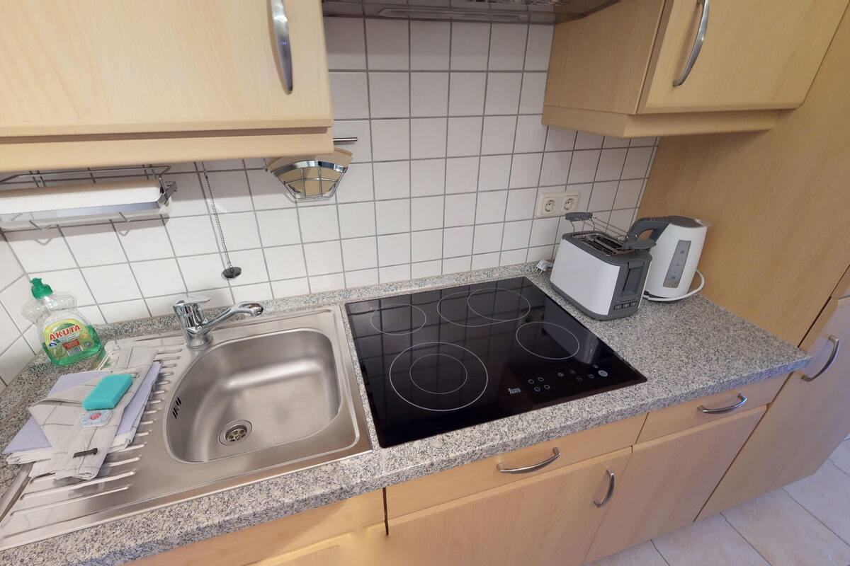 A kitchen with a stainless steel sink, a black induction cooktop, a toaster, and wooden cabinets.