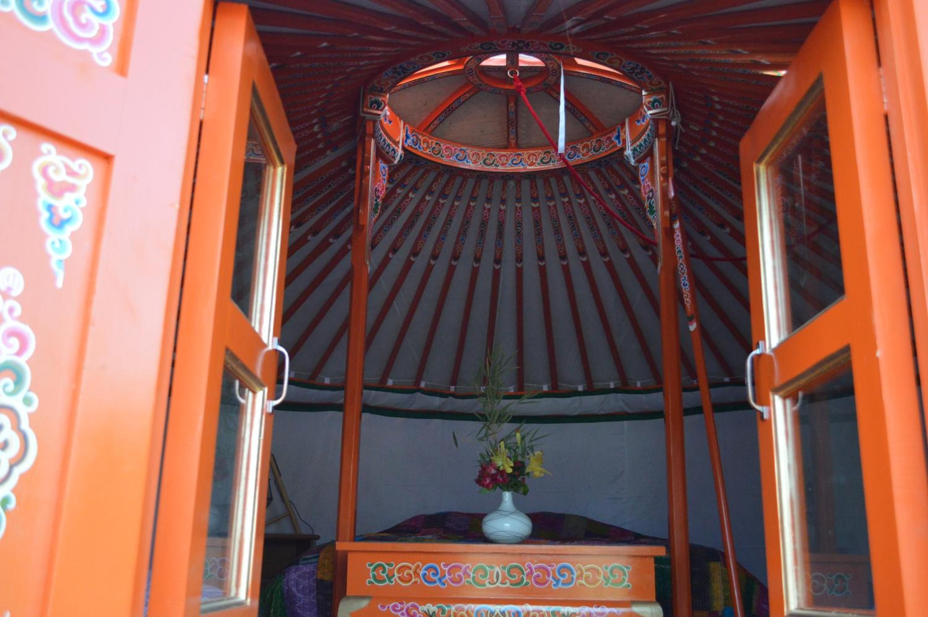 Una habitación tradicional con una cama de dos plazas bajo dosel, una mesita con un florero y decoraciones ornamentales en las paredes.