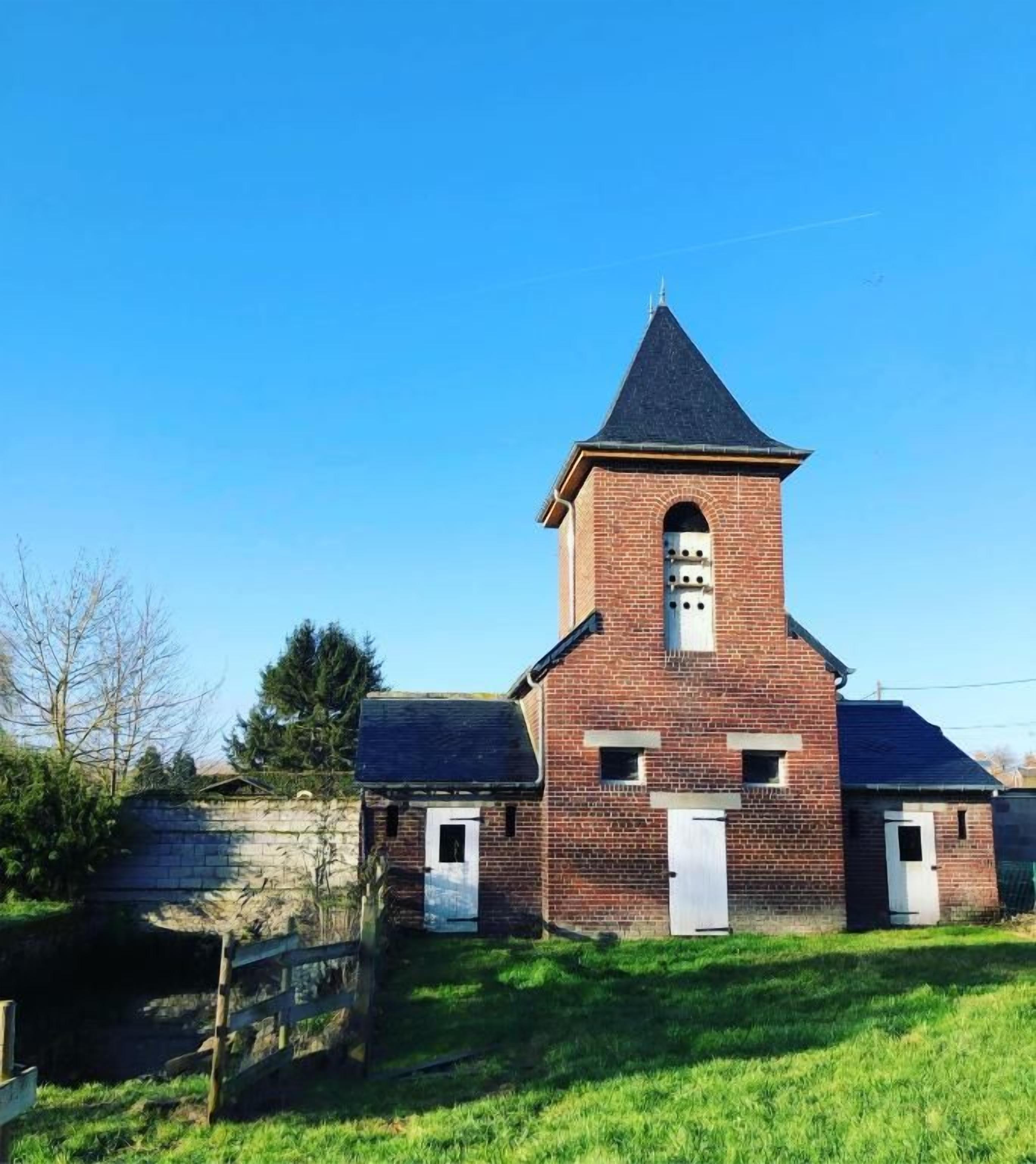 A brick church with a bell tower, a small entrance, and a grassy area in front.