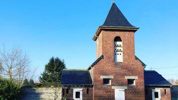 A brick church with a bell tower, a small entrance, and a grassy area in front.