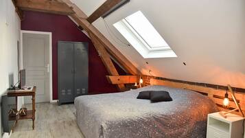 A bedroom with a sloped ceiling, a skylight, a bed with a patterned cover, a wardrobe, a bedside table, and a nightstand with a lamp.