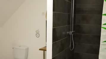 Une salle de bain avec des toilettes blanches, une douche aux carreaux foncés et une petite étagère décorée d’un ananas.