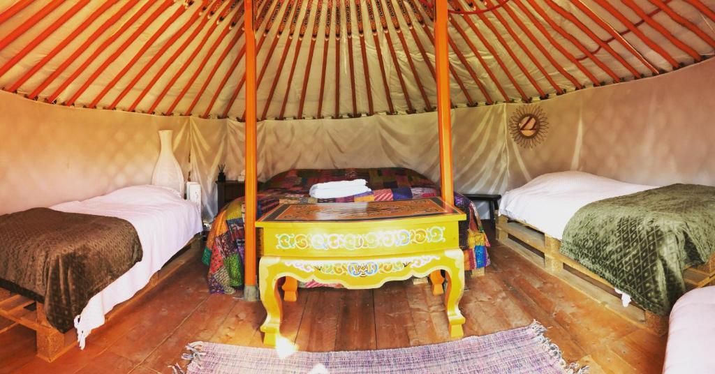 A traditional yurt with a four-poster bed, a wooden table, and two single beds.