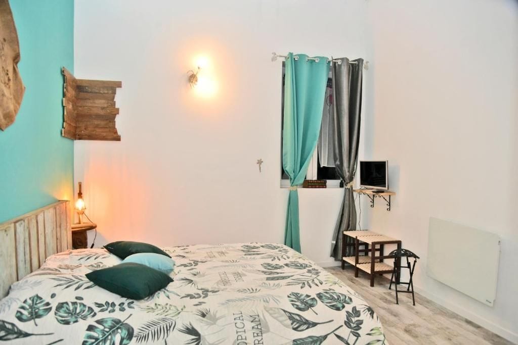 A bedroom with a bed, a desk, a chair, a window with curtains, and a wall-mounted light fixture.