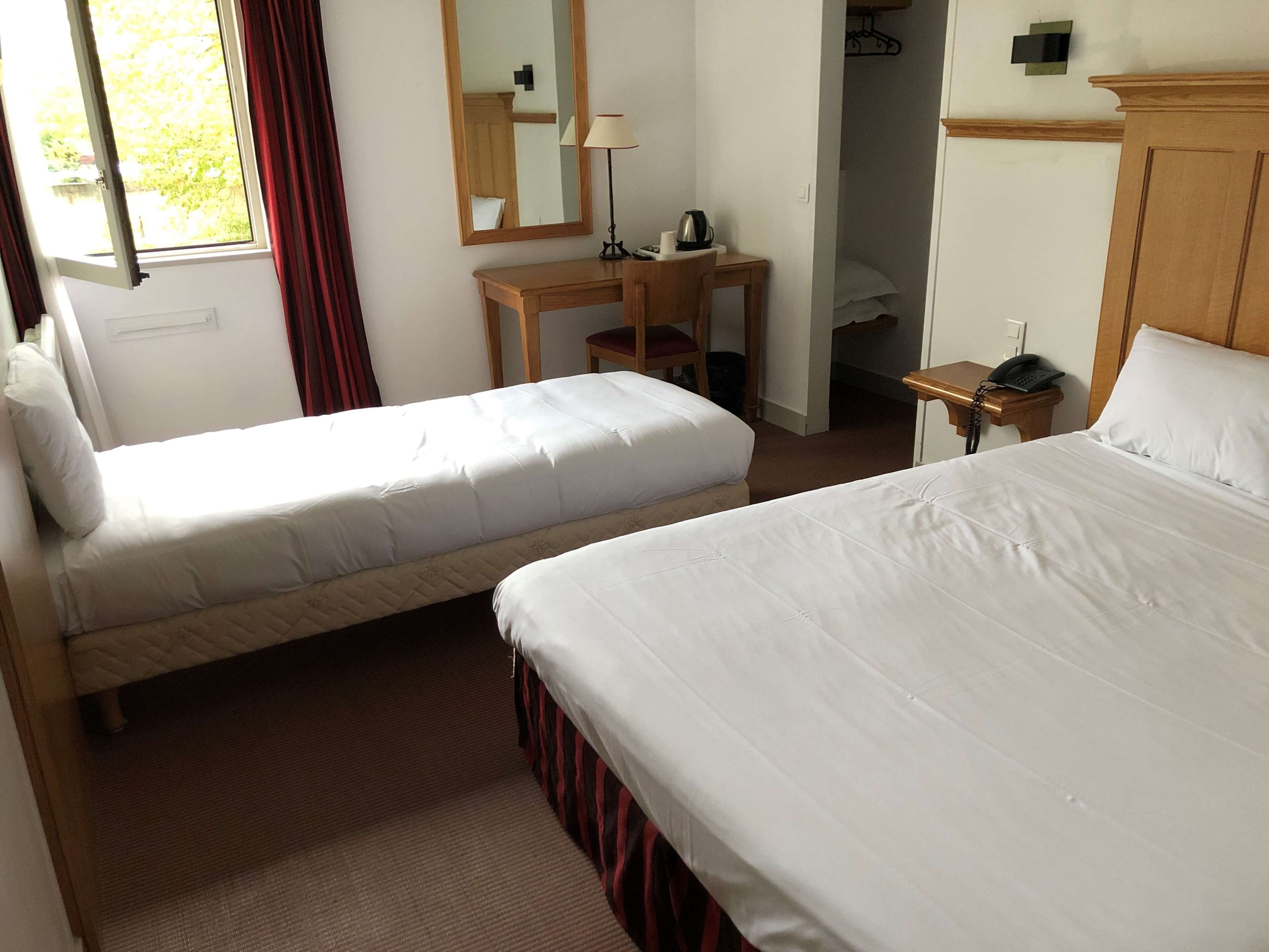 A hotel room with two single beds, a wooden desk with a chair, a telephone, and a mirror on the wall.