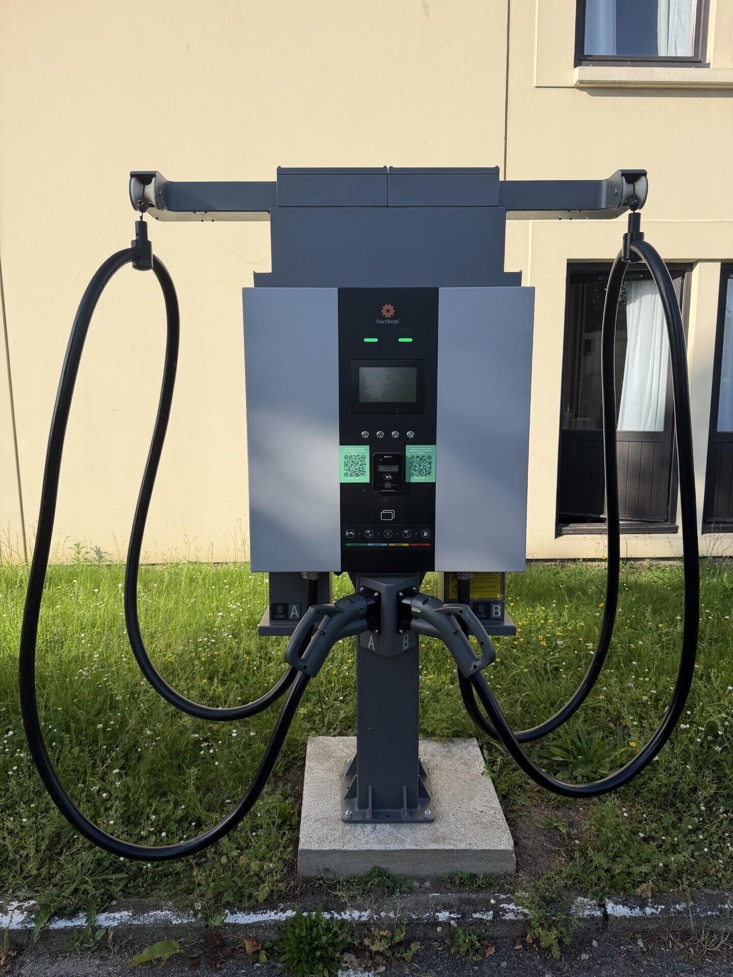A public electric vehicle charging station with a control panel, two charging ports labeled A and B, and a cable connected to the station.