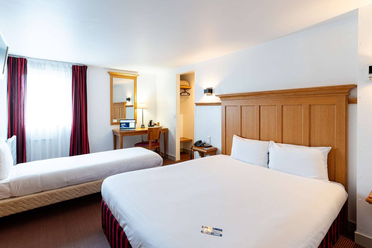 A hotel room with two beds, a desk with a computer, a chair, a nightstand with a phone, and a mirror.