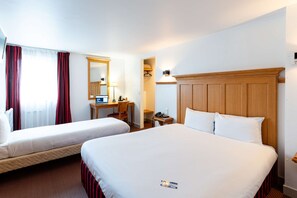 Een hotelkamer met twee bedden, een bureau met een computer, een stoel, een nachtkastje met een telefoon en een spiegel.