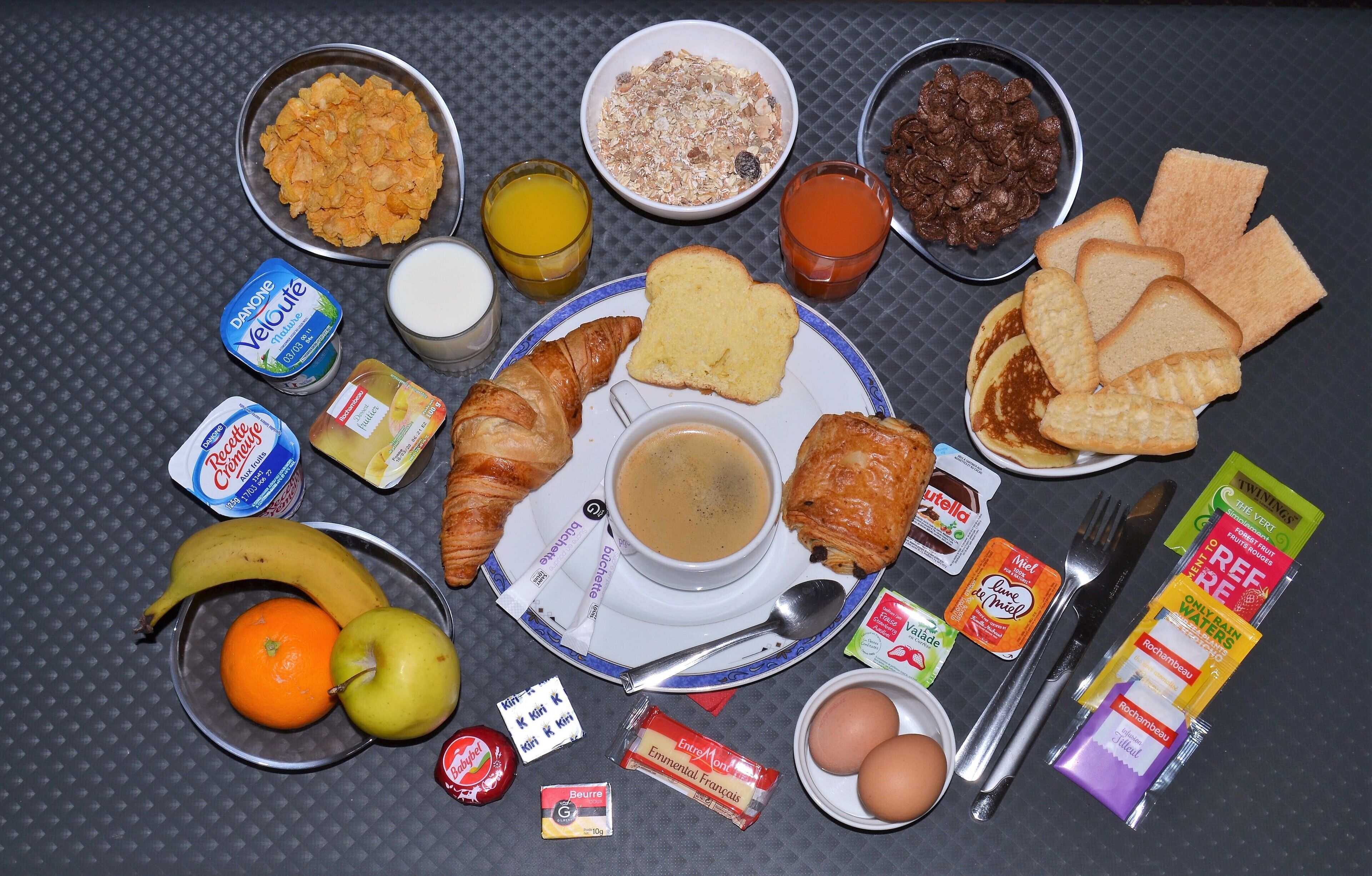 A breakfast table with various food items, including cereal, toast, eggs, and fruit.