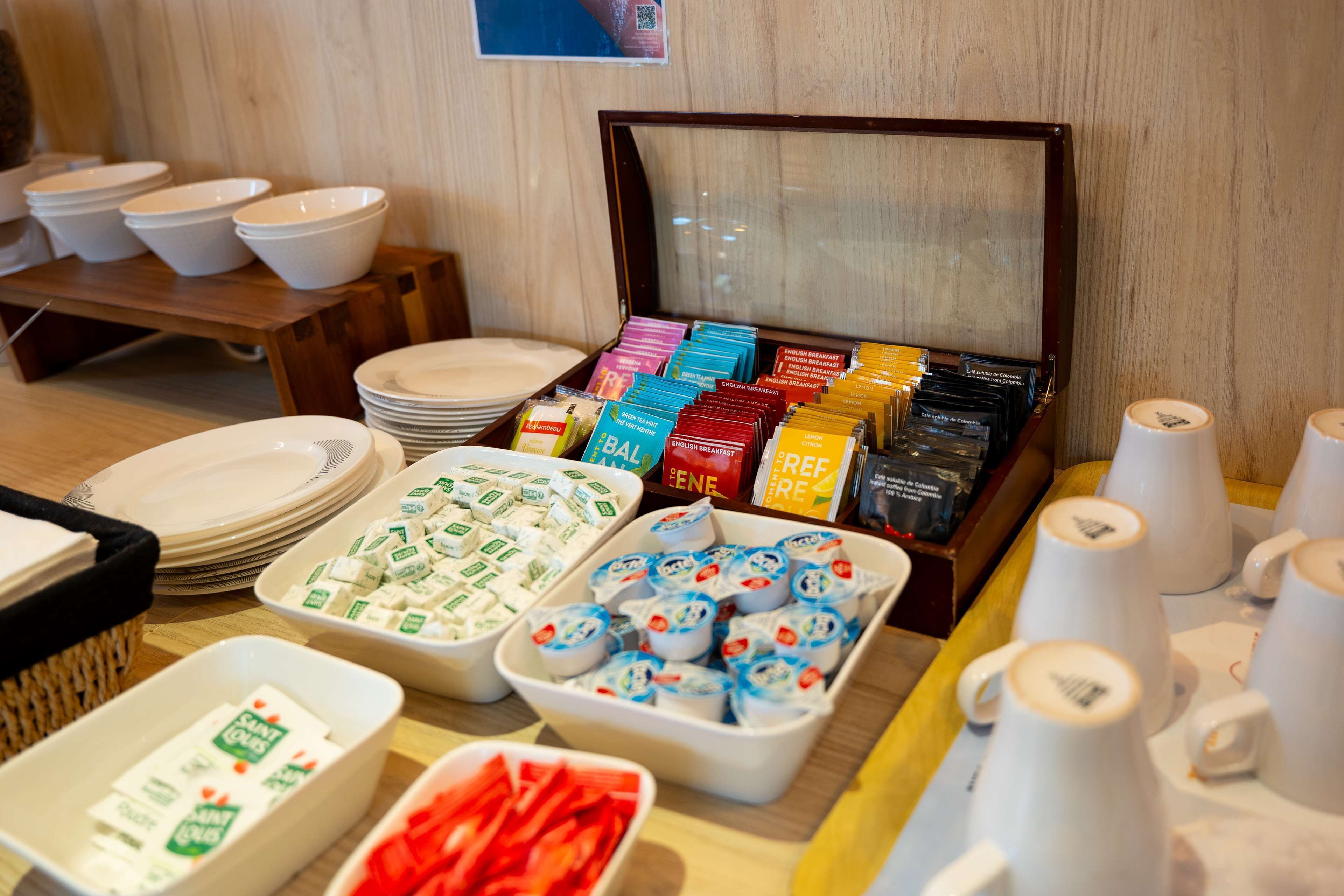 Disposición de un bufé con diferentes opciones de comida, incluyendo yogur, cereales y frutas.