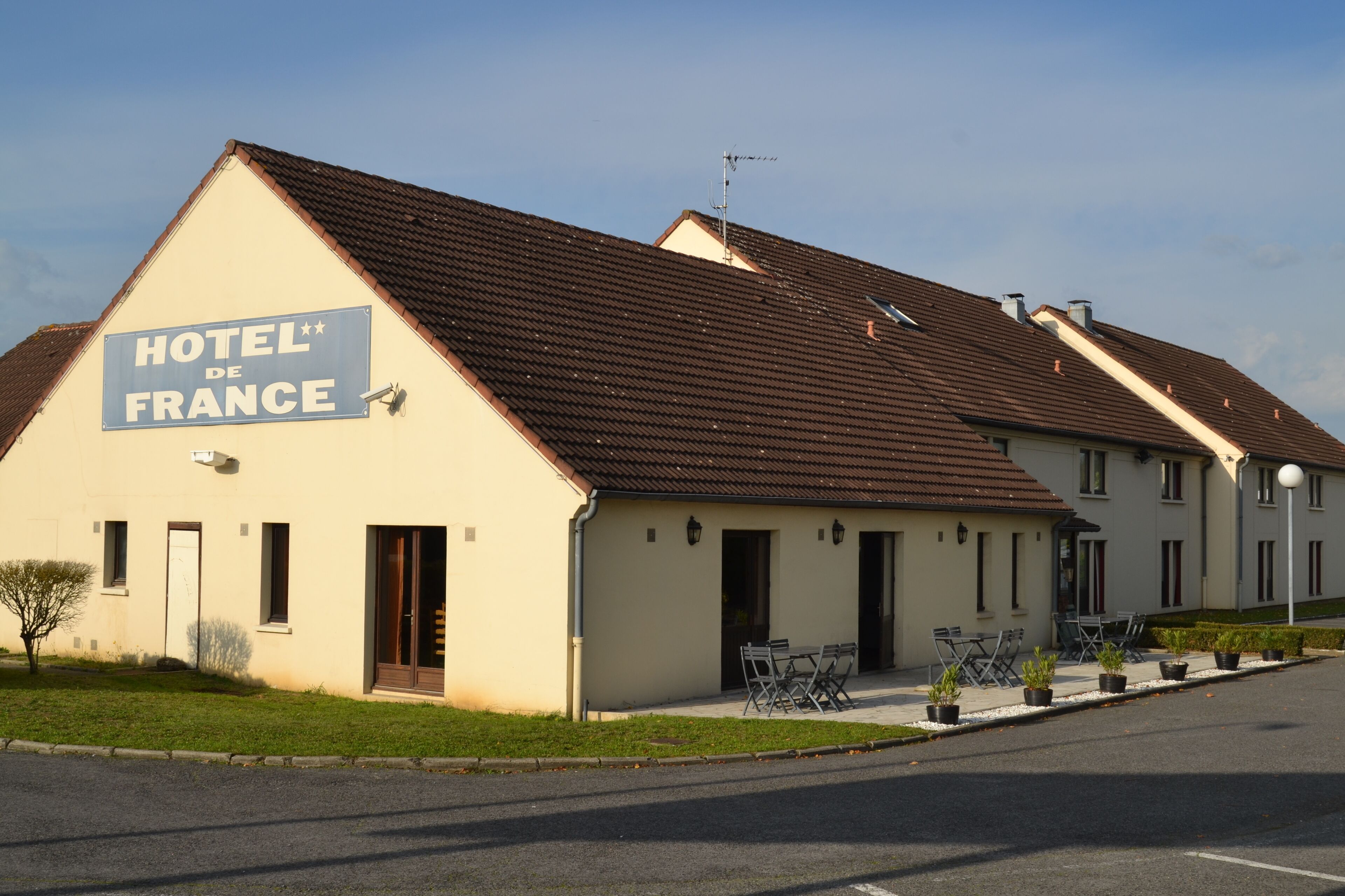 A hotel named "HOTEL DE FRANCE" with a brown tiled roof, a signboard, and outdoor seating.