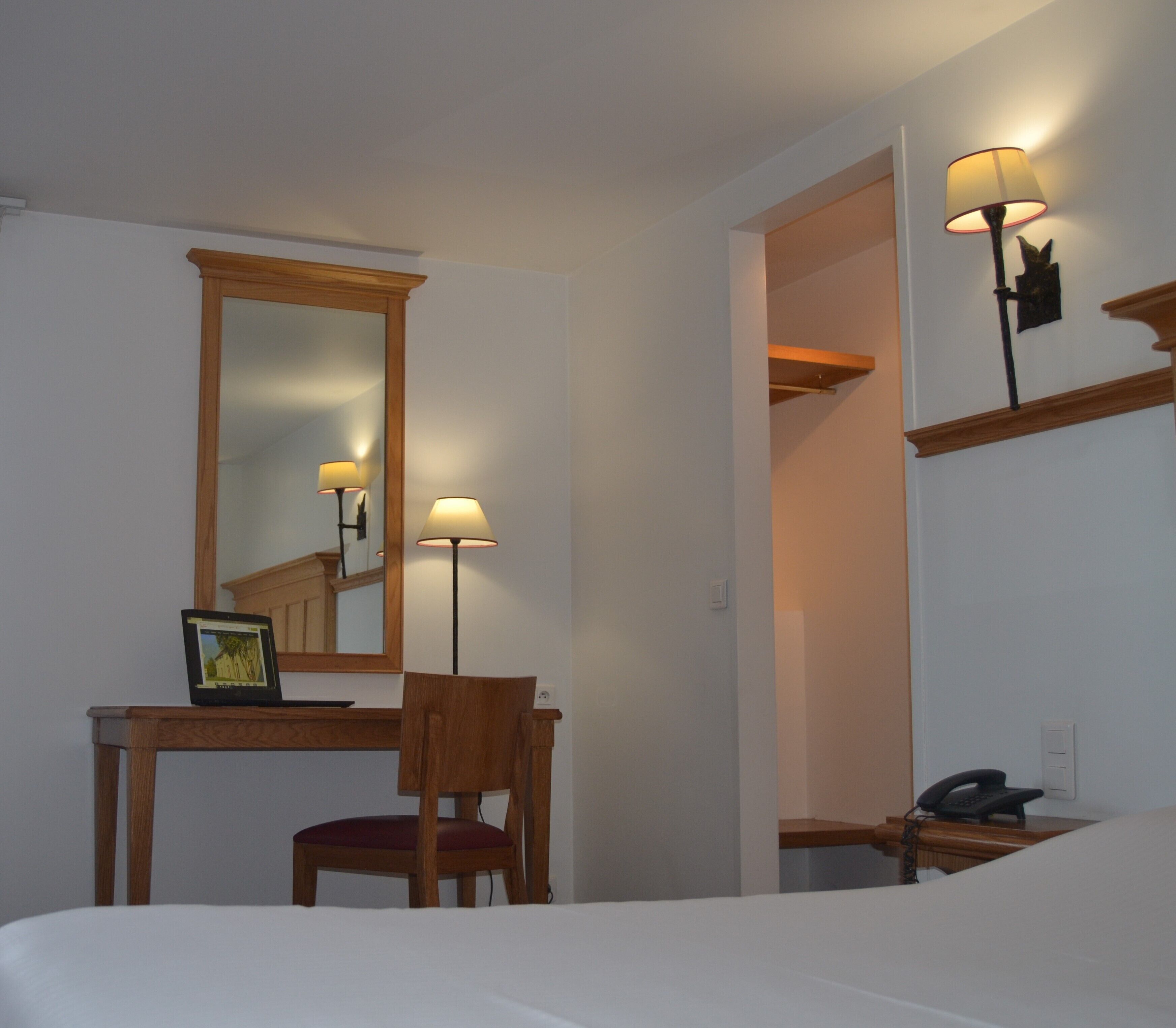 Une chambre d’hôtel comprenant un lit, un bureau avec une chaise, un miroir et deux lampes fixées au mur.