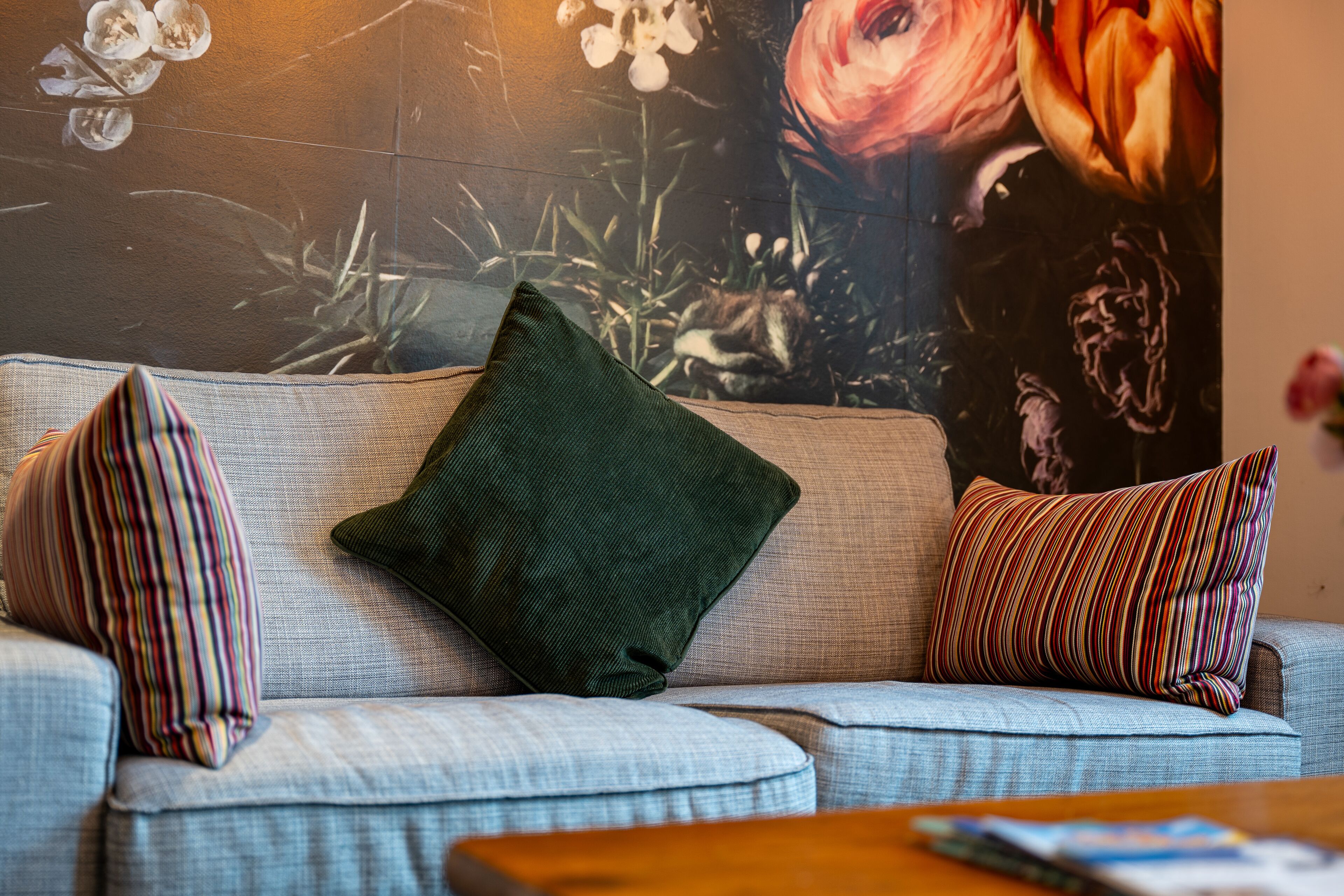 Una sala de estar con un sofá, almohadas a rayas y un cuadro grande con motivos florales en la pared.