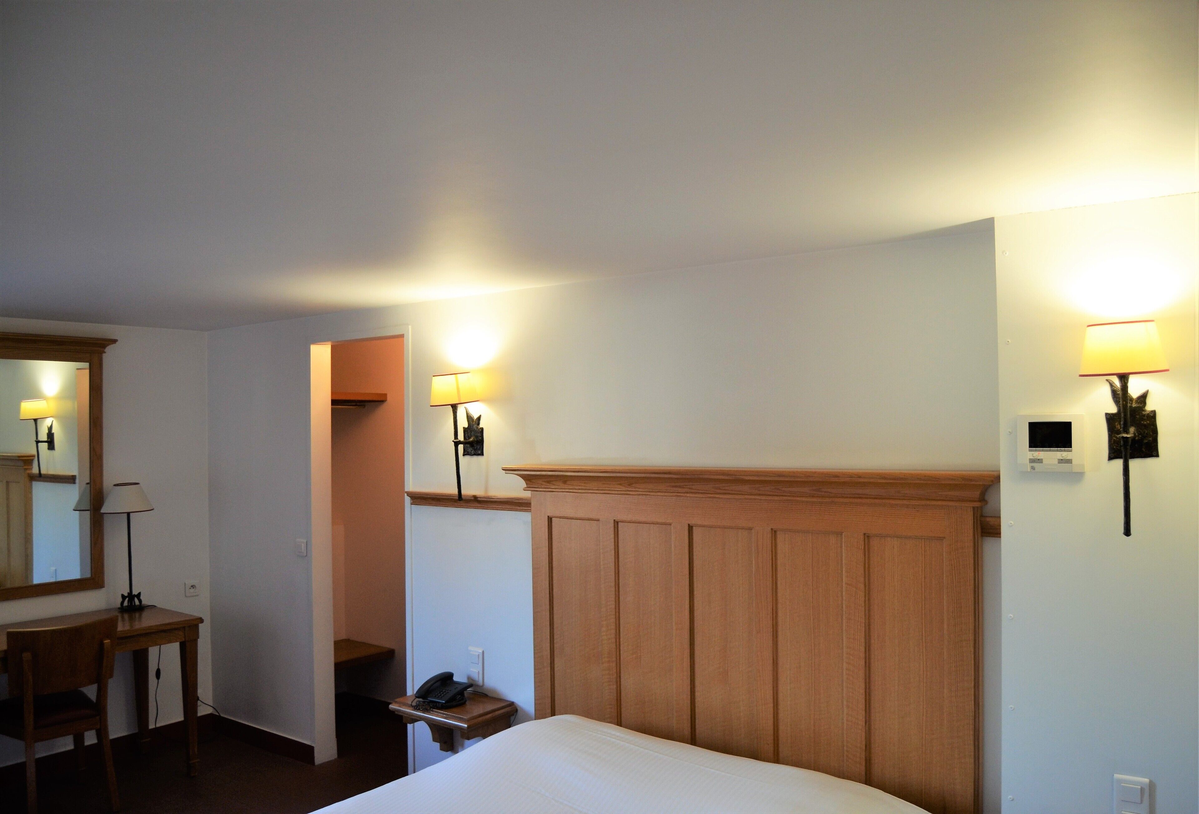 A hotel room with a bed, a desk, a chair, a phone, and two wall-mounted lamps.