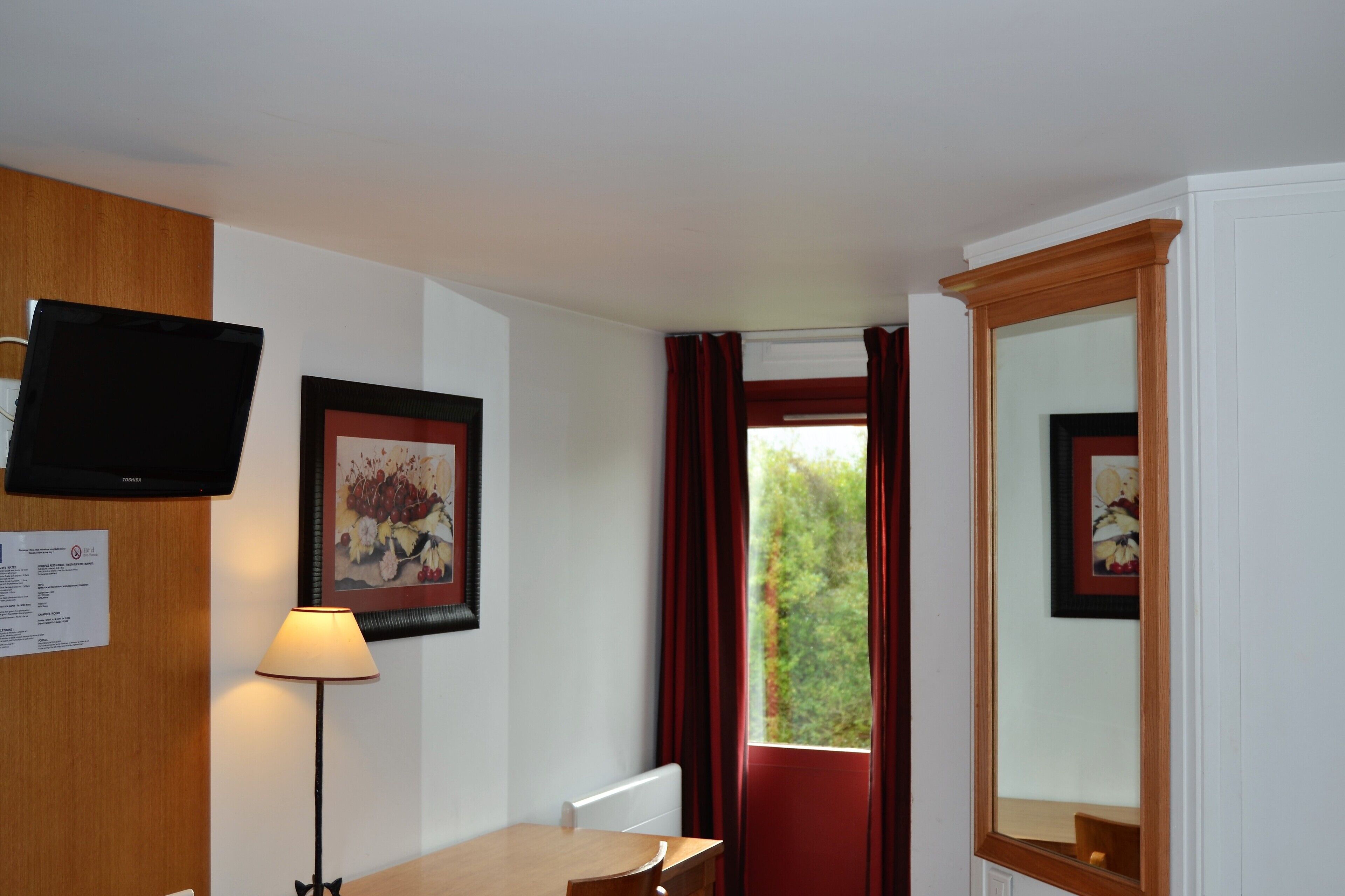 Habitación de hotel con un escritorio de madera, una lámpara, un televisor y un espejo grande.
