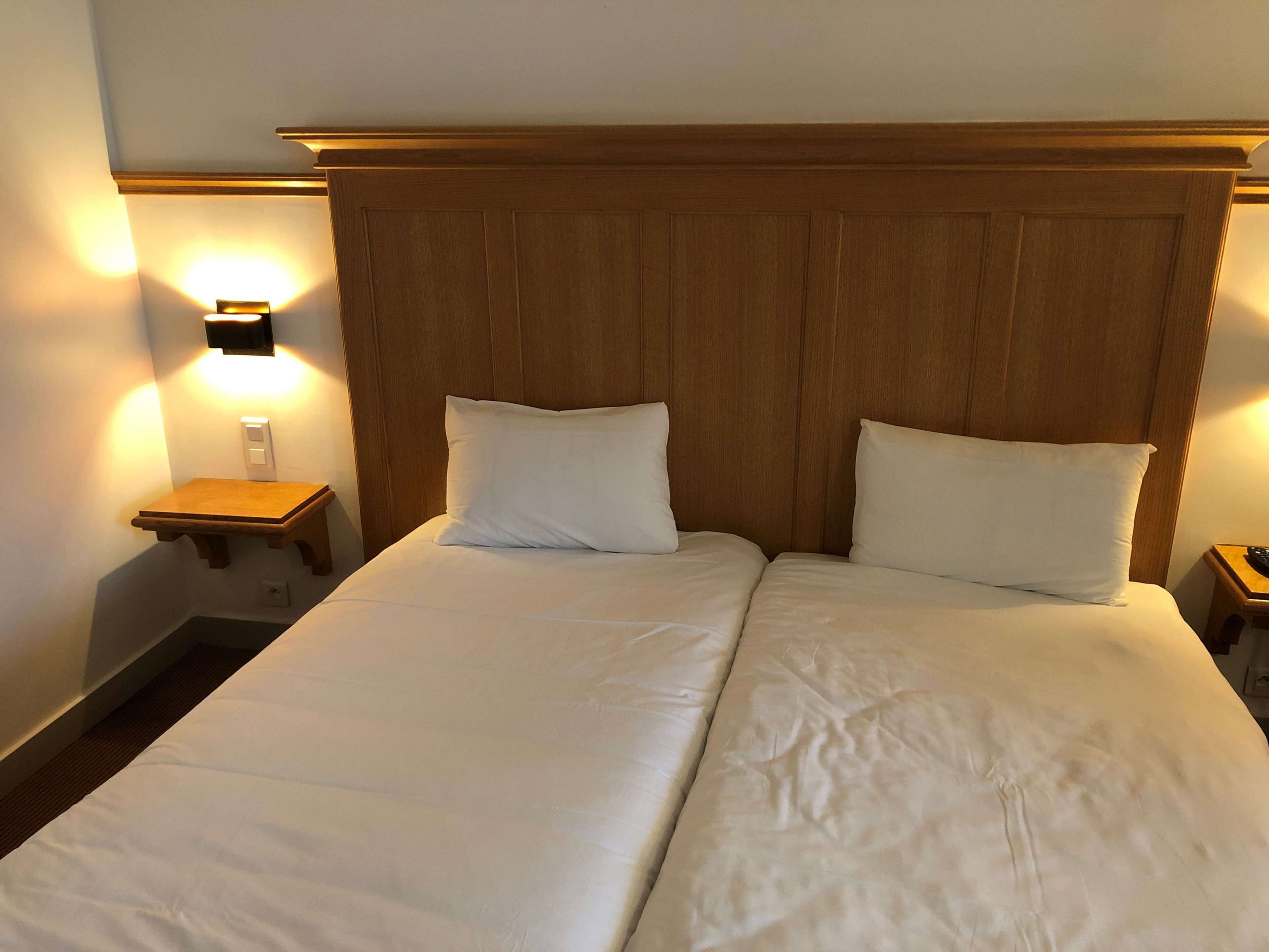 A double bed with a wooden headboard, two bedside tables with lamps, and a wall-mounted light fixture.