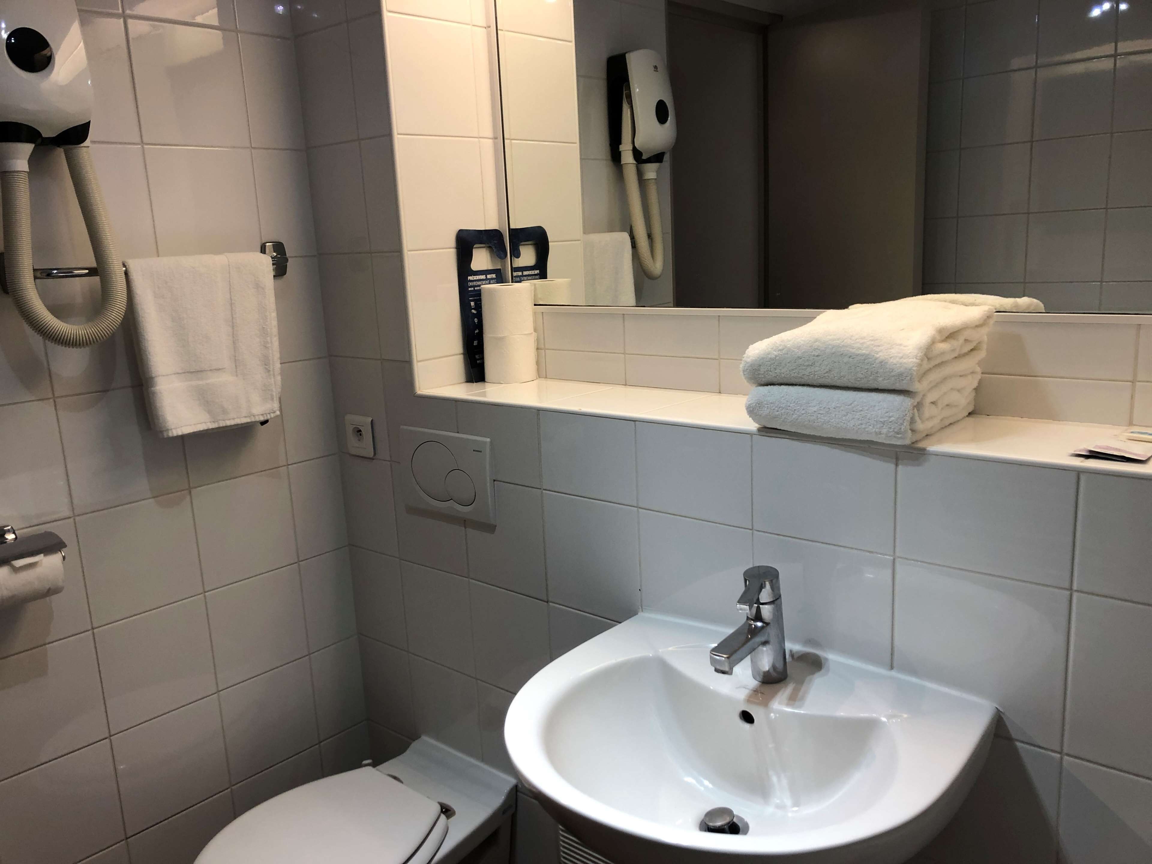 Een badkamer met een witte wastafel, toilet, handdoekhouder, handdroger en spiegel.