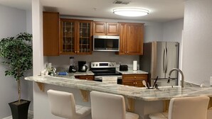 Una cocina moderna con armarios de madera, un refrigerador de acero inoxidable, un microondas integrado y una isla de mármol con taburetes de bar.