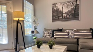 Una sala de estar moderna con un sofá gris, almohadones a rayas, una mesa de centro blanca y una lámpara de pie negra.