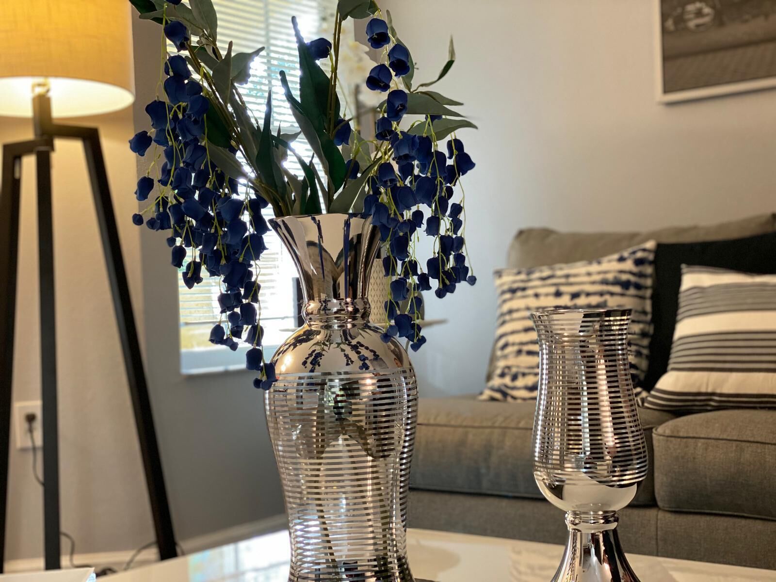 A living room with a glass vase containing blue flowers, a lamp, and a sofa with striped cushions.