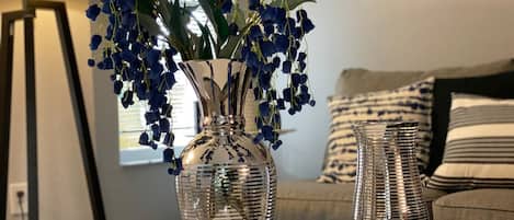 A living room with a glass vase containing blue flowers, a lamp, and a sofa with striped cushions.