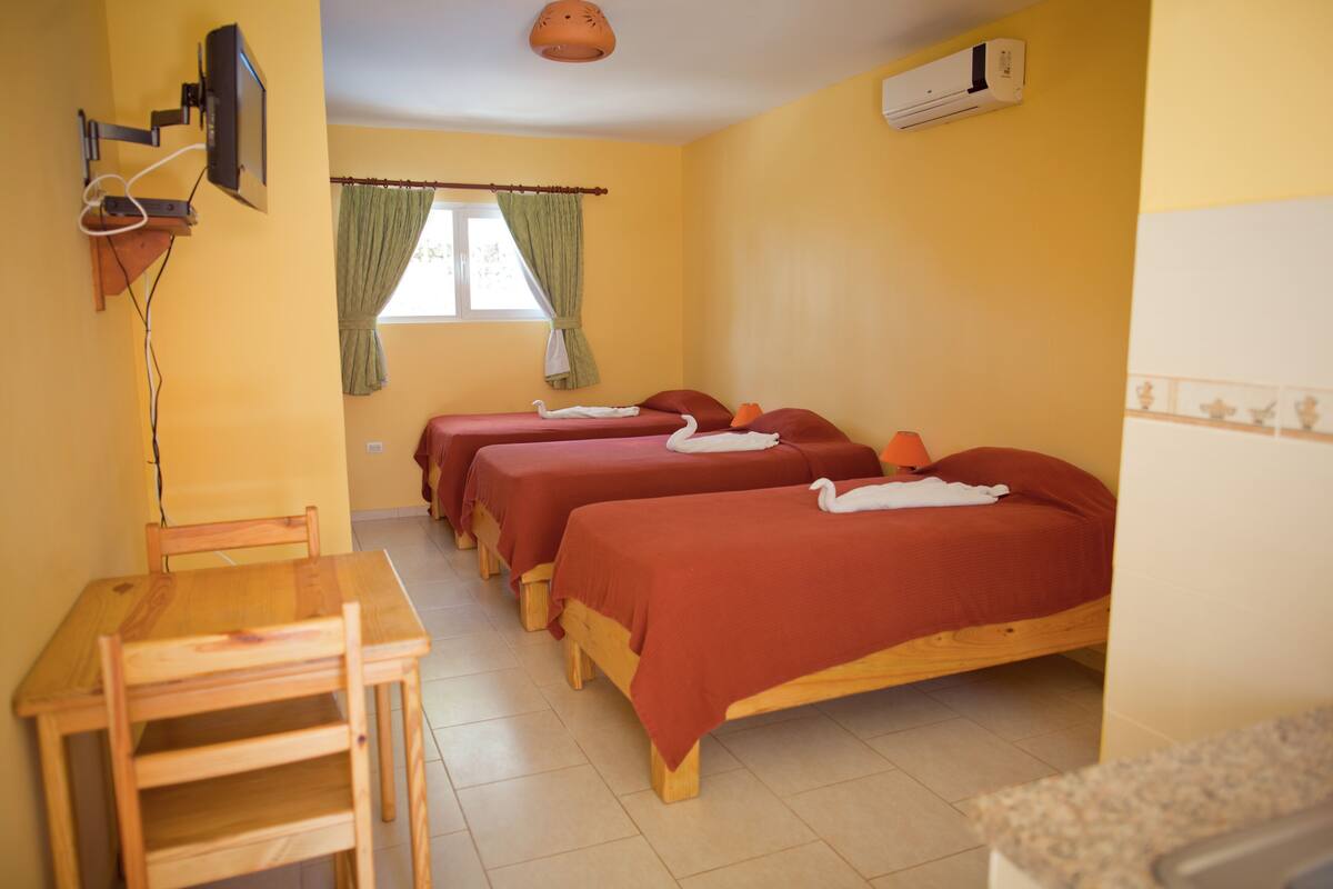 A room with three wooden beds, a wooden table, and a television mounted on the wall.