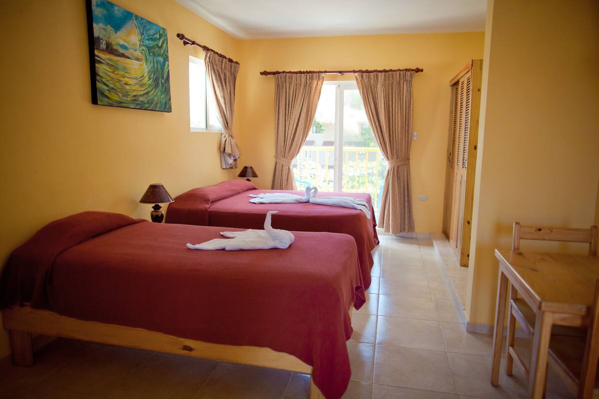 A hotel room with two beds, a wooden chair, a small table, and a painting on the wall.