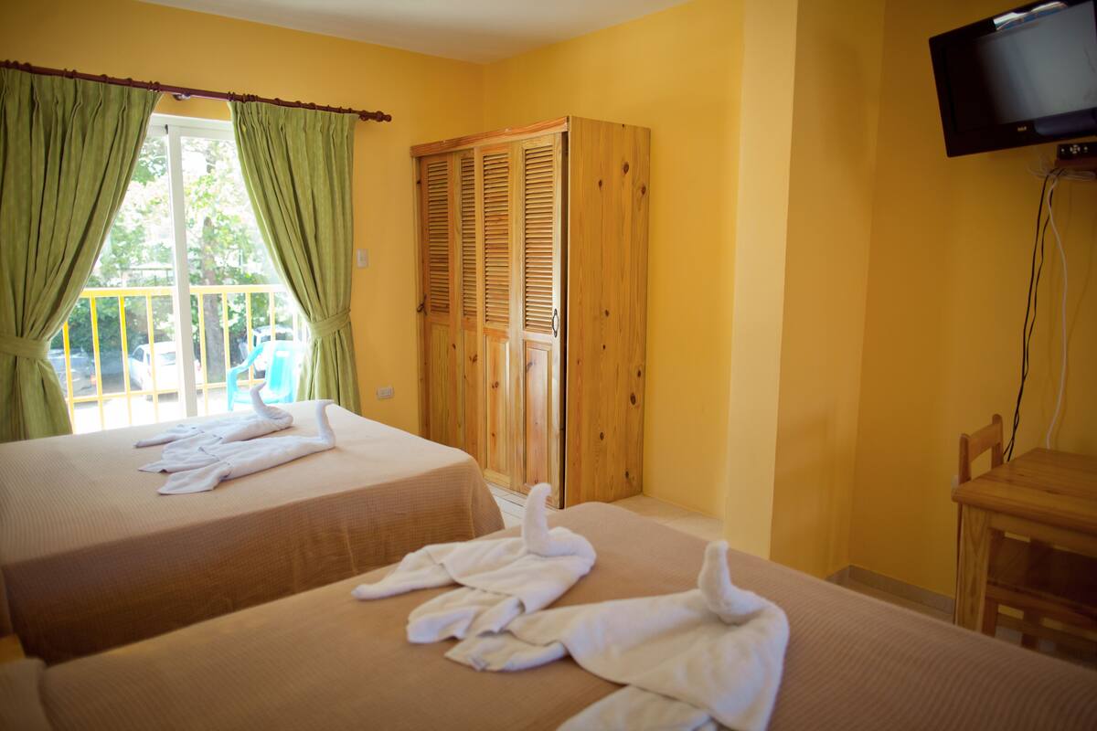 A hotel room with two beds, a wooden wardrobe, a television, and a balcony with a view.