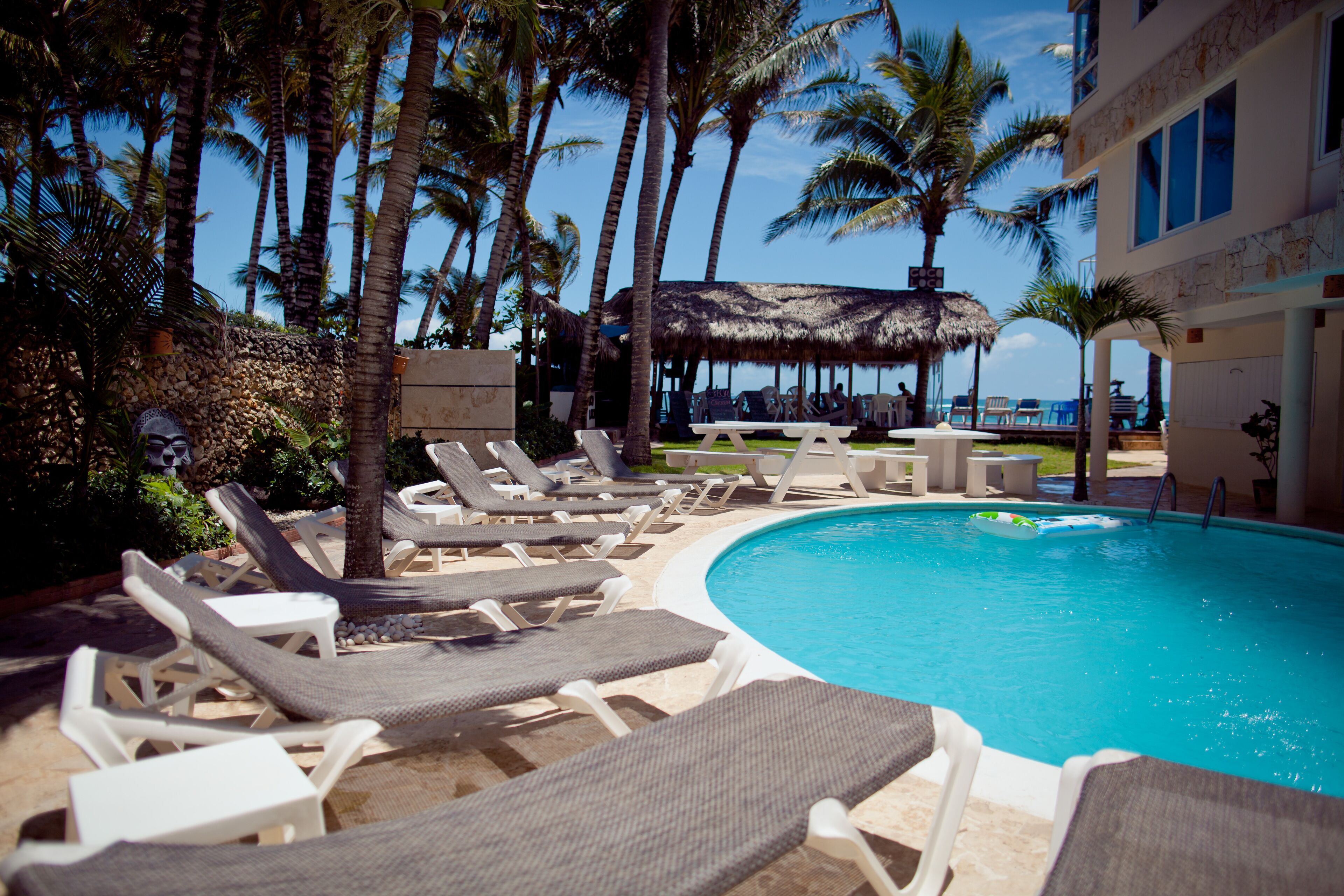 A poolside area with lounge chairs, a thatched-roof structure, and palm trees.