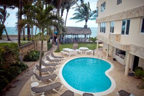 A swimming pool with lounge chairs, a thatched-roof structure, and a view of the ocean. - Kite Beach Inn (Cabarete)