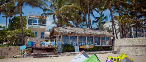 A beachside hotel with a thatched-roof structure, palm trees, and a sign for the "Kite Beach Inn."