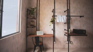 Une pièce au décor minimaliste, avec un bureau en bois, une chaise noire, une plante en pot, une étagère avec une pancarte et un radiateur.