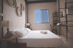 A bedroom with a bed, a nightstand, a lamp, a window, and a shelf with plants. - Tranquil Nest Vaavu Maldives (Rakeedhoo)