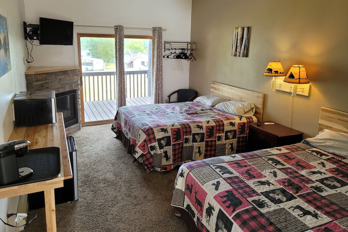 A bedroom with a fireplace, a desk, a bed with a quilt, and a balcony with curtains.