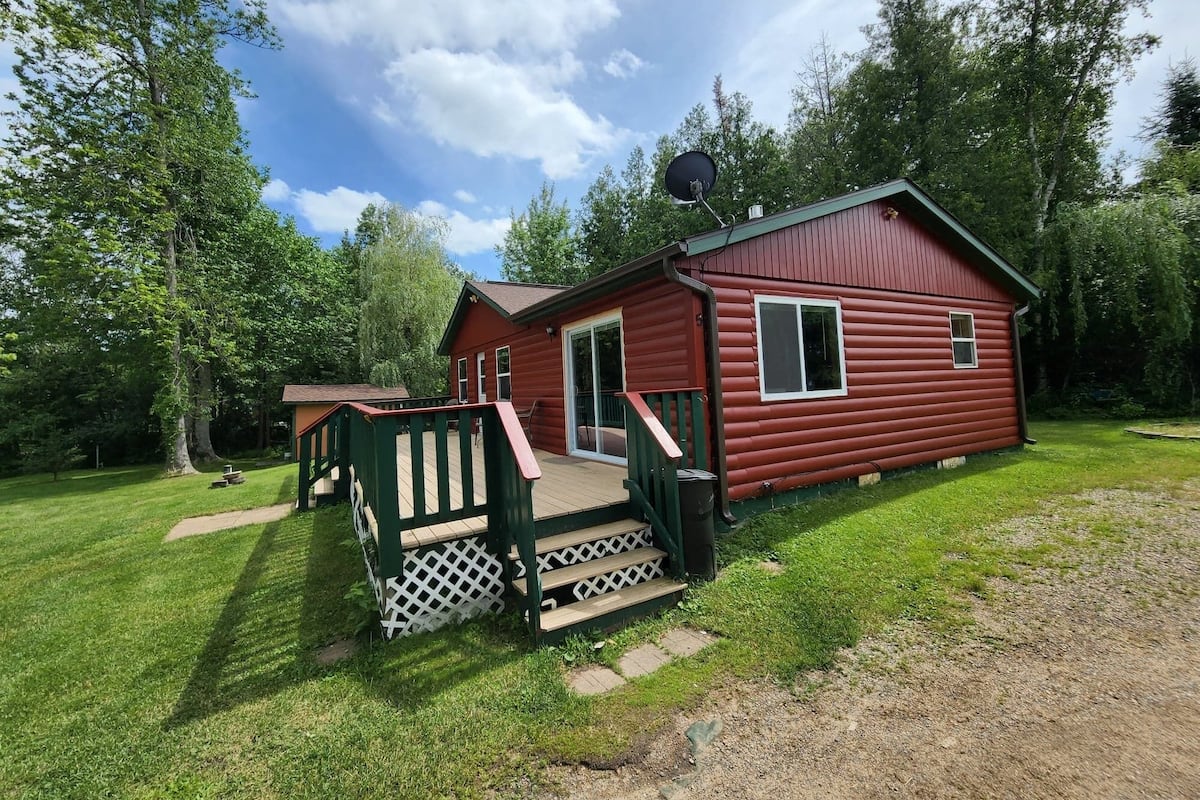 A red cabin with a deck and a satellite dish, surrounded by trees.