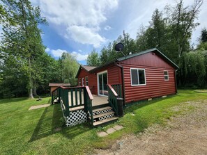 A red cabin with a deck and a satellite dish, surrounded by trees. - Blue Moon Resort and Motel (Hill City)