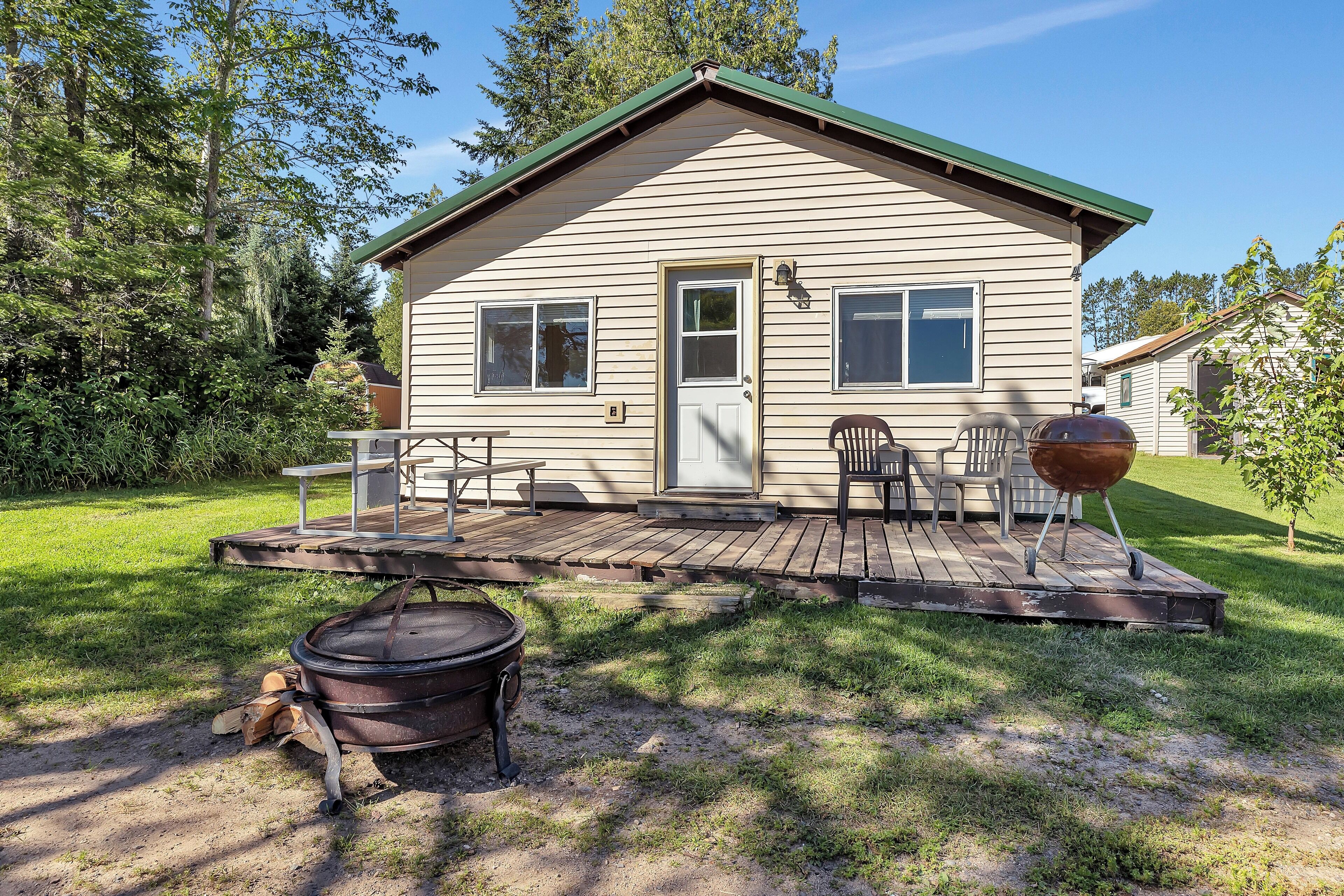 A small, single-story cabin with a deck, outdoor seating, and a grill.