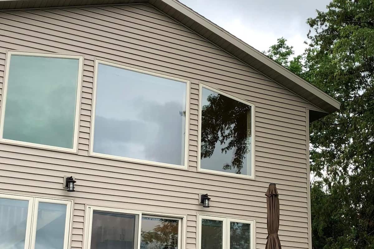 A two-story house with large windows, a patio with chairs and an umbrella, and a visible door.