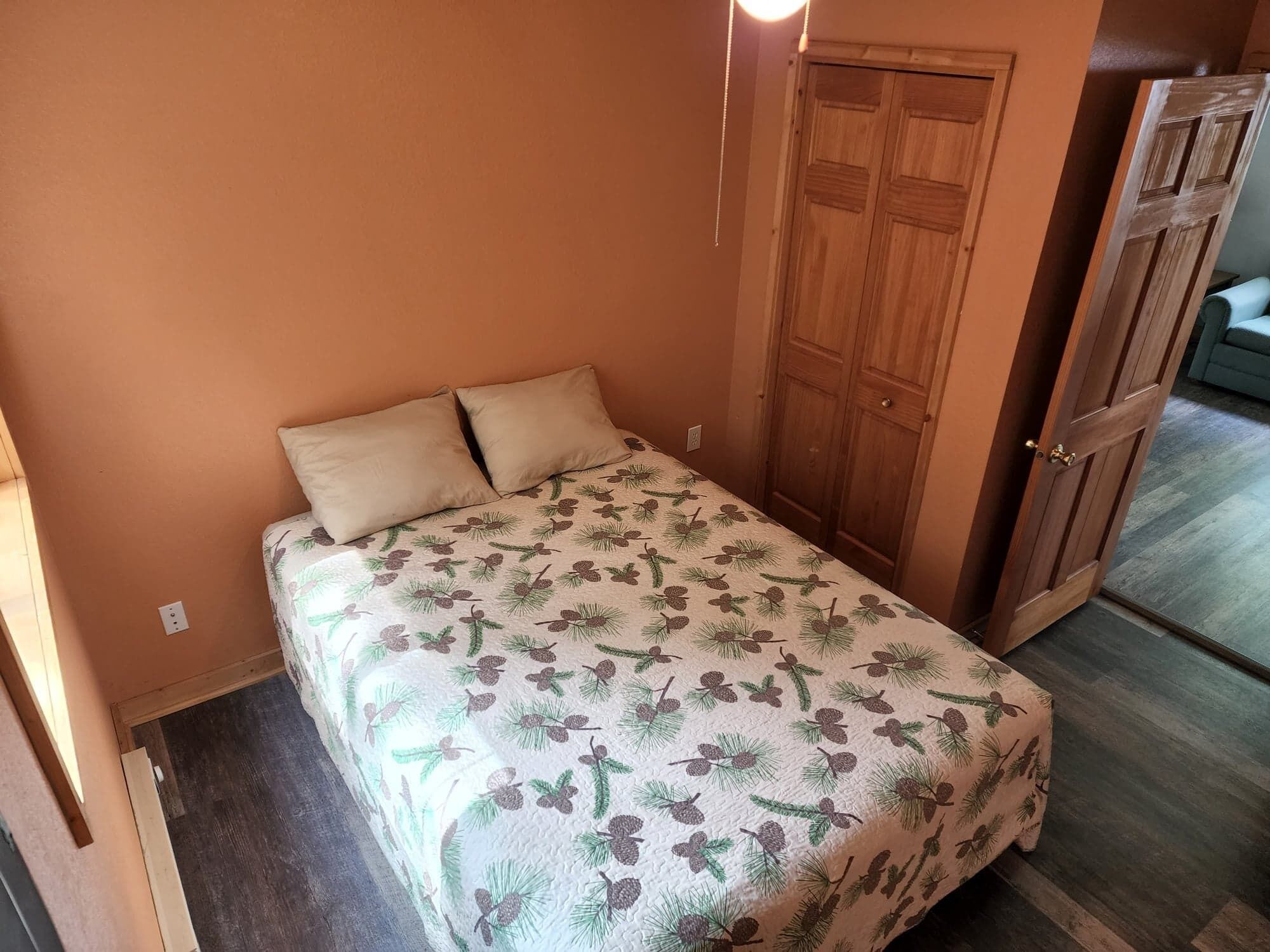 Une petite chambre à coucher, chaleureuse et accueillante, avec un lit, deux oreillers, une armoire en bois et une porte.