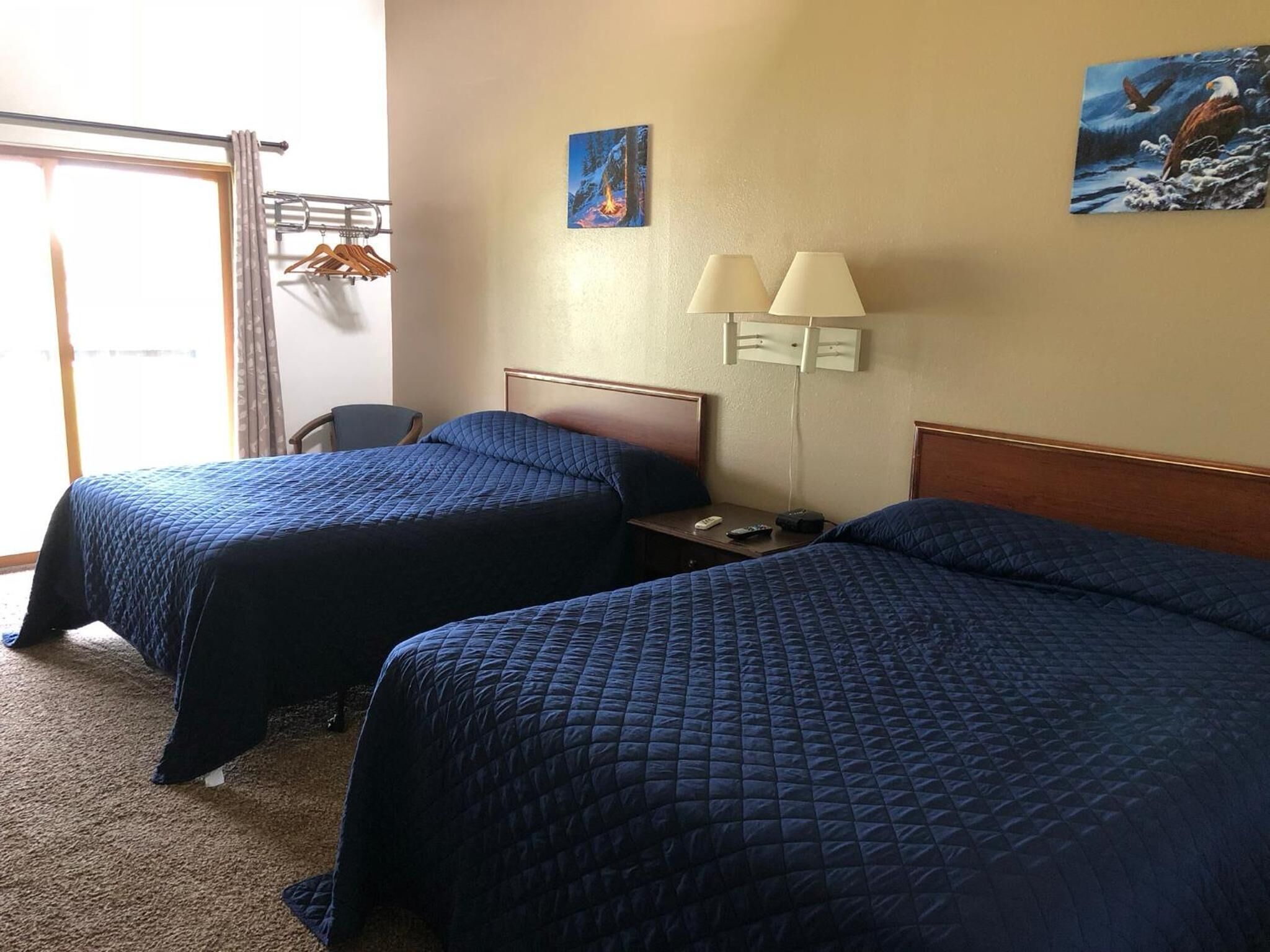 A hotel room with two beds, a desk, a chair, and a window with curtains.