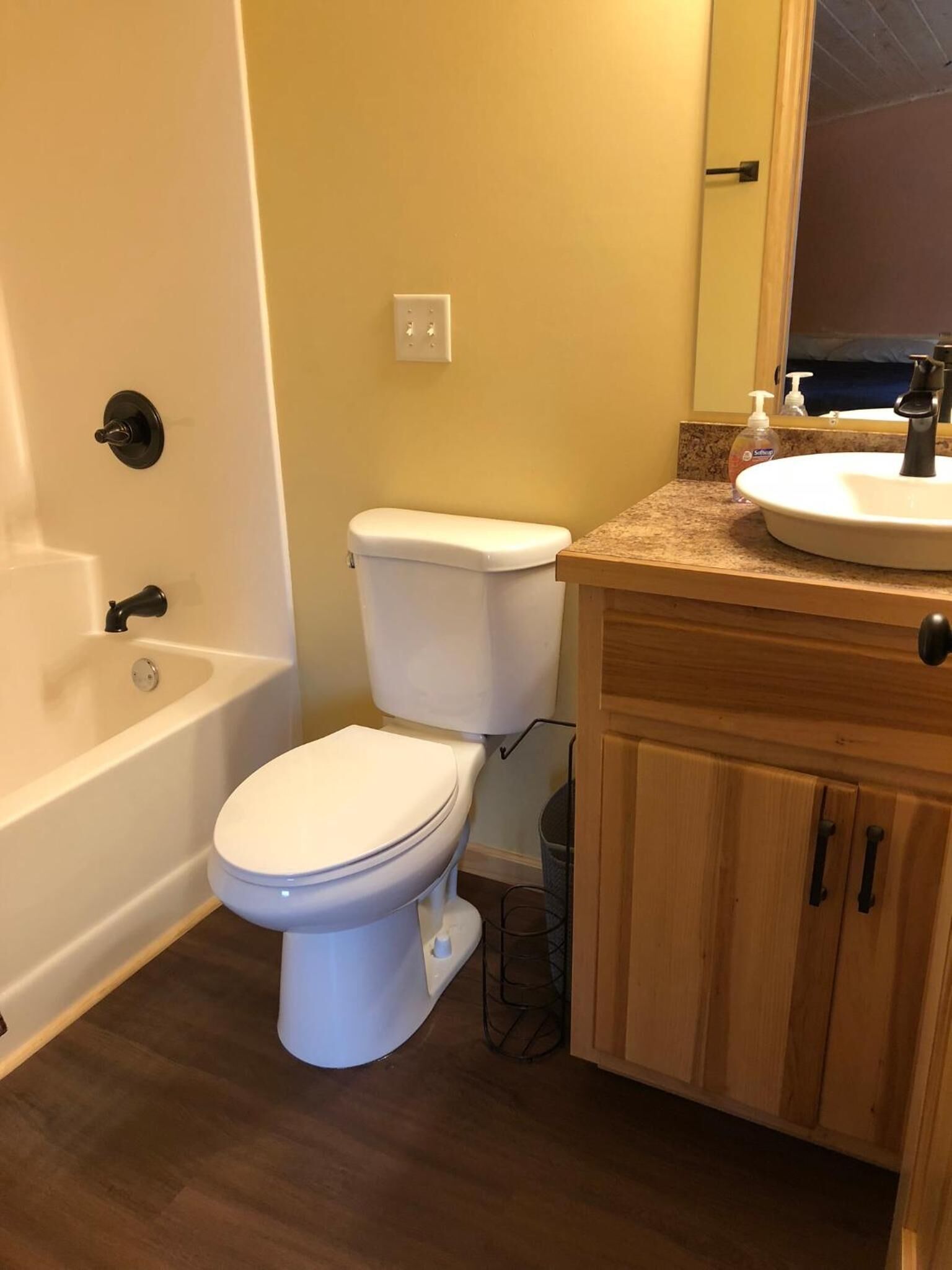 Un baño con inodoro blanco, bañera, lavamanos con espejo y armarios de madera.